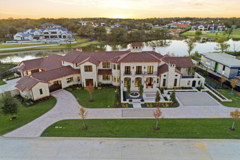 Wide aerial dusk view of the full estate property with pool, motor court, and surrounding grounds aglow beneath a deep violet and amber evening sky