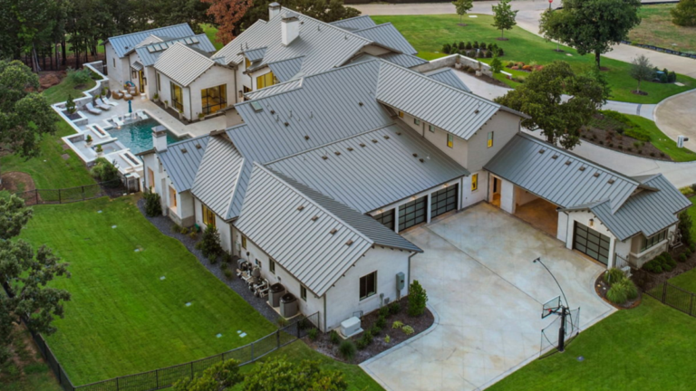 Aerial view of a luxury custom home with metal roofing, multiple rooflines, and a backyard pool on a landscaped property