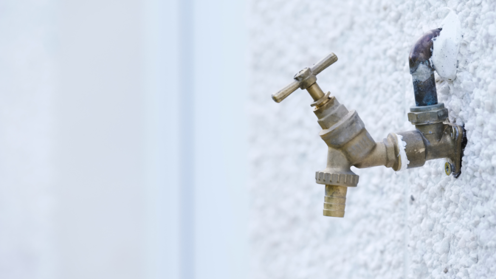 Exterior hose bib mounted on a stucco wall, a common freeze-risk location requiring protection in cold weather.