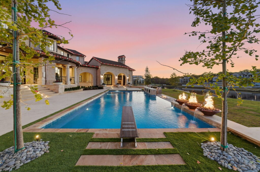 Luxury custom estate in Westlake featuring a long resort-style pool with fire features, stone patio, and covered outdoor living area at sunset.
