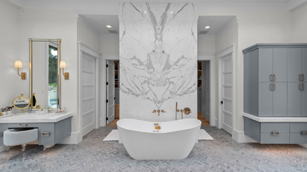 White and gray marble master bath with a vanity on the left and two walk-in closets on either side of the tub.