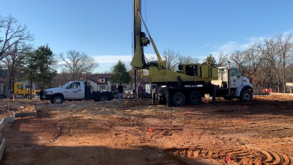 Excavator and craftsmen on residential jobsite with trucks and large crane to dig piers.
