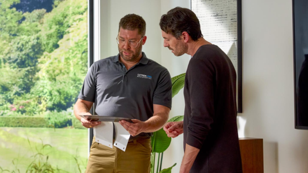 Lutron technician reviewing smart home lighting plan with homeowner inside modern residential interior.