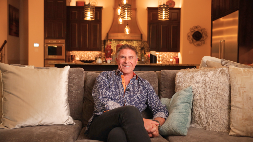 Man sitting on couch smiling at camera inside the living room of his luxury estate renovated by Garabedian Properties.