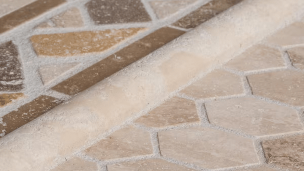 A close-up of travertine mosaic flooring showing tan, brown, and cream stone tiles in an irregular pattern with visible grout lines.