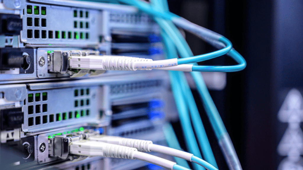 Close-up of fiber optic and ethernet cables connected to network switches in a server rack inside a smart home, with green status lights illuminated.