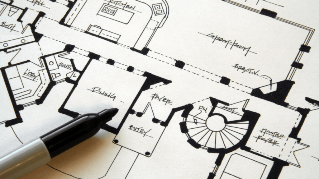 Custom home plan set and specification pages spread across a table with handwritten revision notes in the margin.
