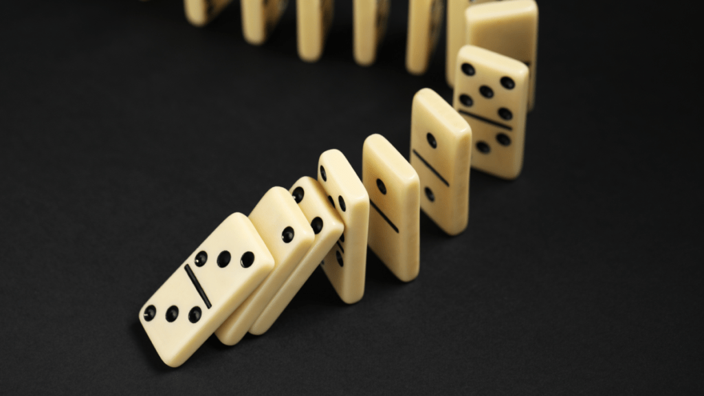Dominoes lined up with one tipping over indicating a cascading effect.