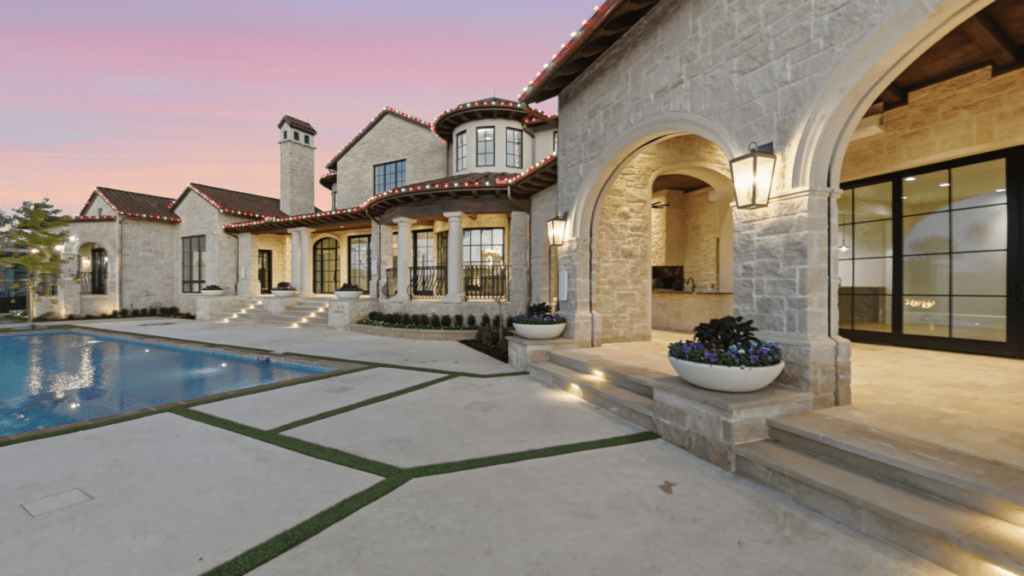 Stone custom estate at dusk with illuminated lantern fixtures, recessed step lighting, and a pool courtyard, built by Garabedian Properties in North Texas.