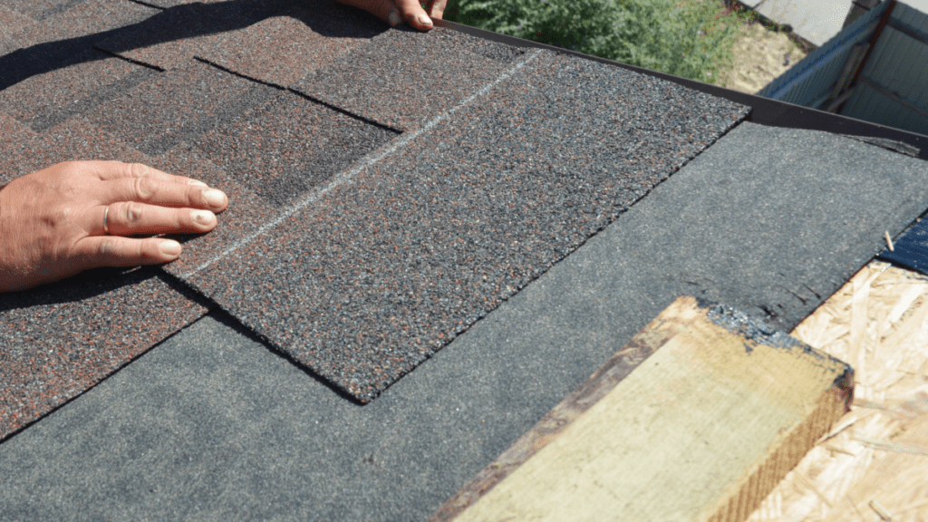 Close-up of hands aligning a new asphalt shingle into place along a roofline during a repair.
