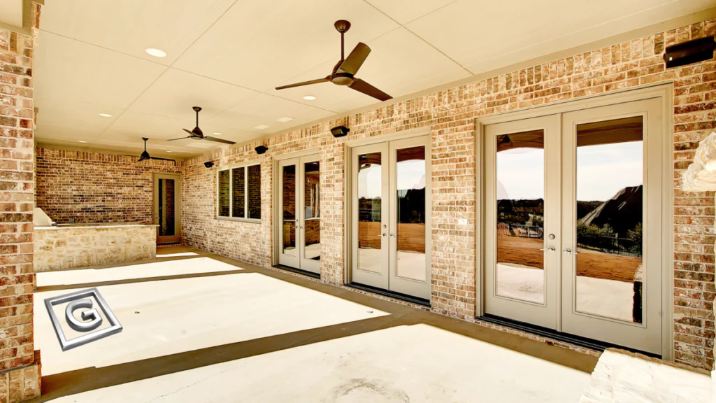 Covered outdoor patio with a brick exterior, multiple glass French doors, and ceiling fans overhead, shown in a warm sepia-toned edit with the Garabedian Properties logo in the corner.