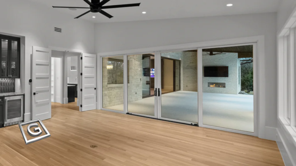Interior room with light wood flooring, a black ceiling fan, a built-in wine fridge and glass cabinetry on the left, and a wide wall of glass sliding doors opening onto a covered patio with a fireplace.